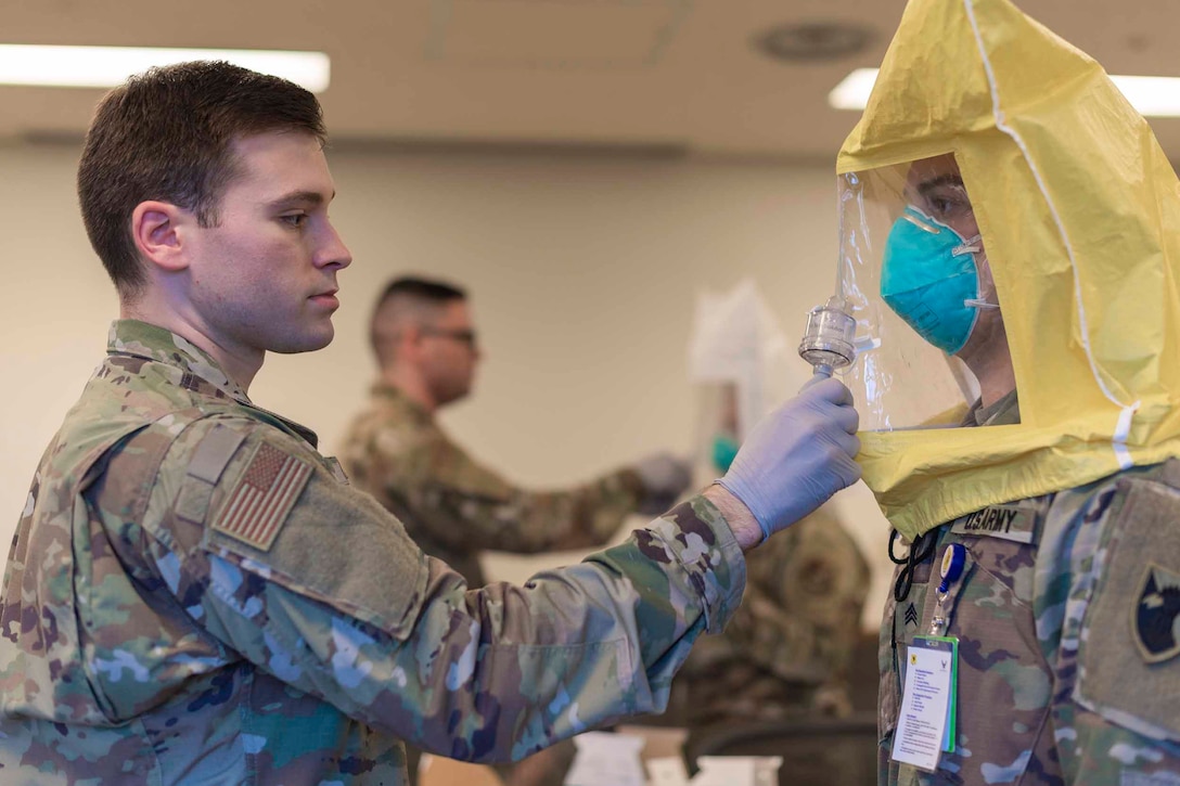 An airman fits a plastic head covering over another airman.