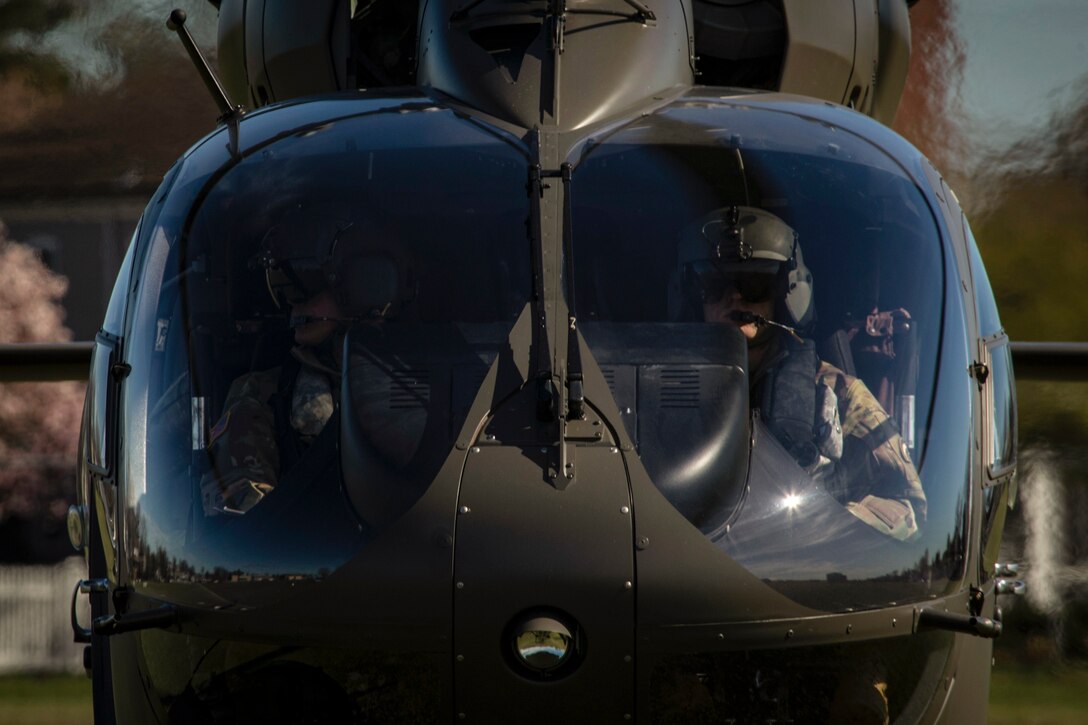 Two soldiers look out from the cockpit of a Lakota helicopter.