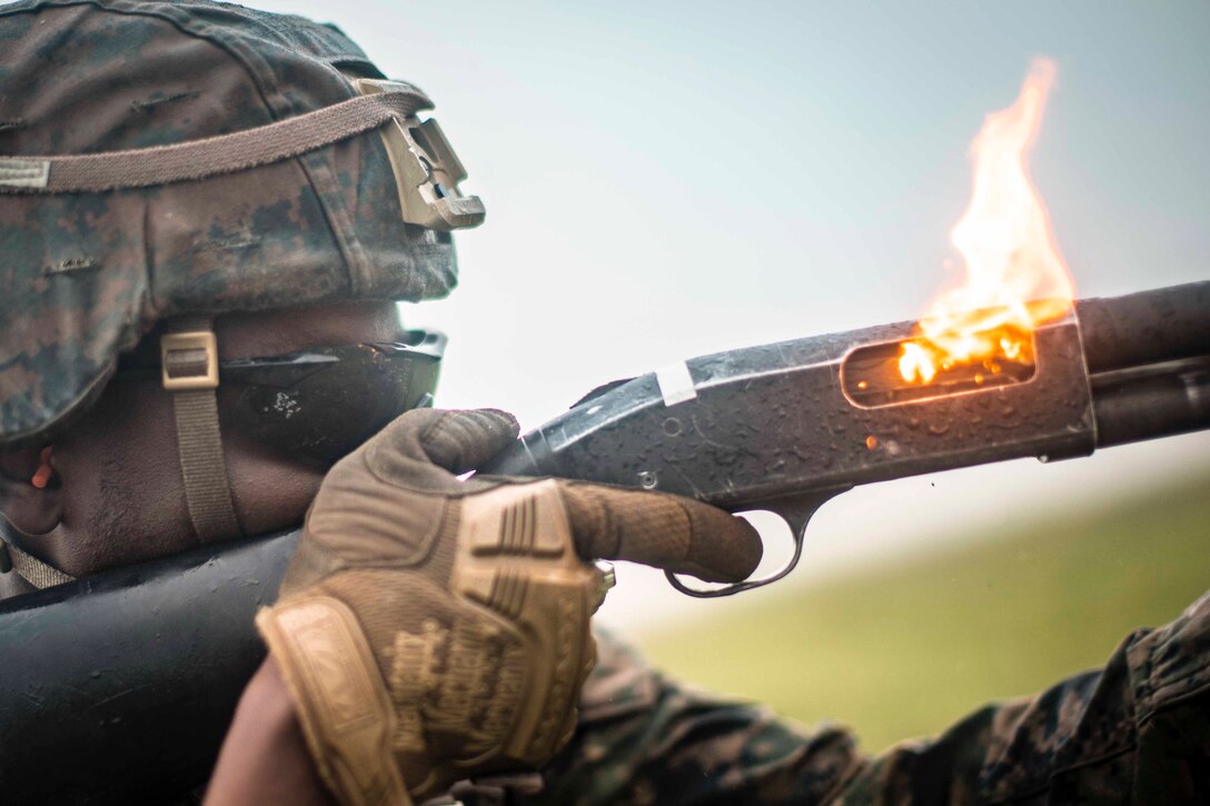 A Marine fires a shotgun with flames coming from the chamber.