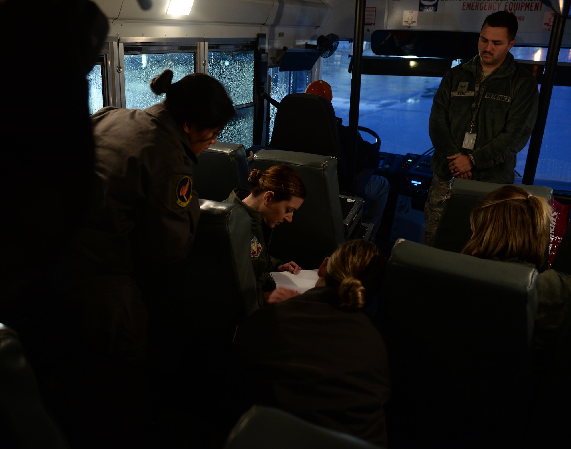 A group of female Airmen looking over a maintenance folder on a bus before departure.