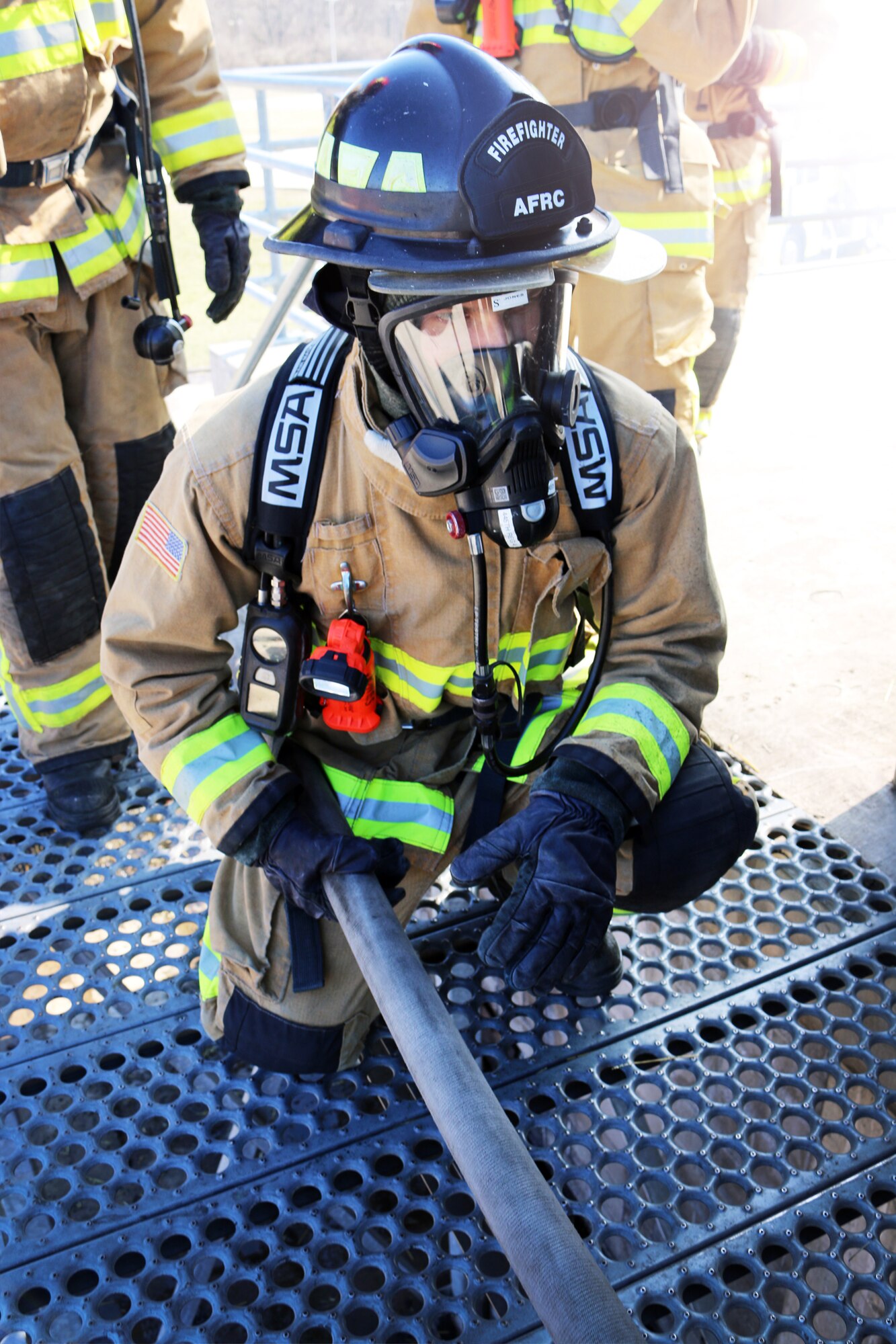 Senior Airman Matthew Archer, firefighter with the 445th Civil Engineer Squadron, Fire and Emergency Services Flight, stabilizes a charged hose while his teammate ahead breaches the door at the Dayton Fire Department training facilities on March 7, 2020. Archer is part of a five-person team honing their communication and maneuvering skills to reach a basement fire in the training building, as part of live structure fire training. (U.S. Air Force photo/1st Lt. Rachel Ingram)