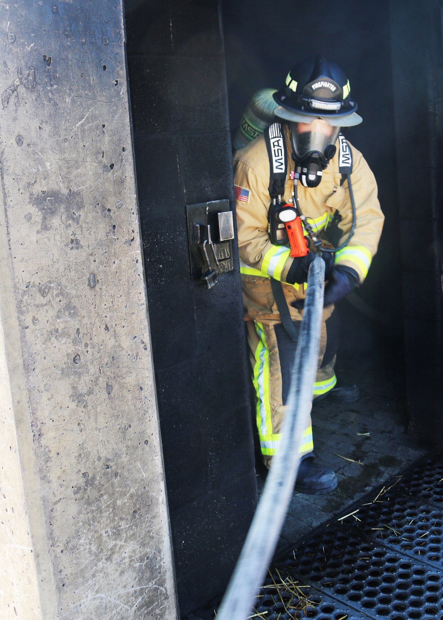 Senior Airman Ryan Guenther, firefighter with the 445th Civil Engineer Squadron, Fire and Emergency Services Flight, feeds a charged hose through an upper-level door at the Dayton Fire Department training facilities on March 7, 2020. Guenther is part of a five-person team honing their communication and maneuvering skills to reach a basement fire in the training building, as part of live structure fire training. (U.S. Air Force photo/1st Lt. Rachel Ingram)