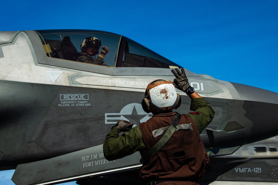 A U.S. Marine signals to the pilot of an F-35B Lightning II fighter aircraft during an air defense exercise on the flight deck of amphibious assault ship USS America (LHA 6), March 22.