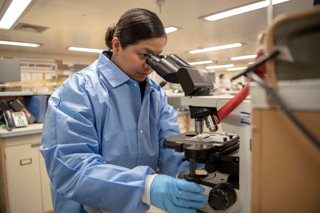 A sailor in protective clothing looks into a microscope.