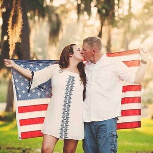Army Soldier and wife kiss while holding U.S. flag