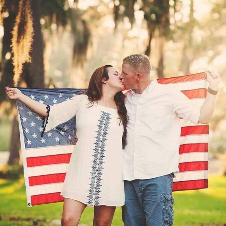 Army Soldier and wife kiss while holding U.S. flag