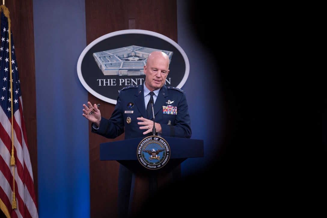 A man in military uniform stands behind a lectern.