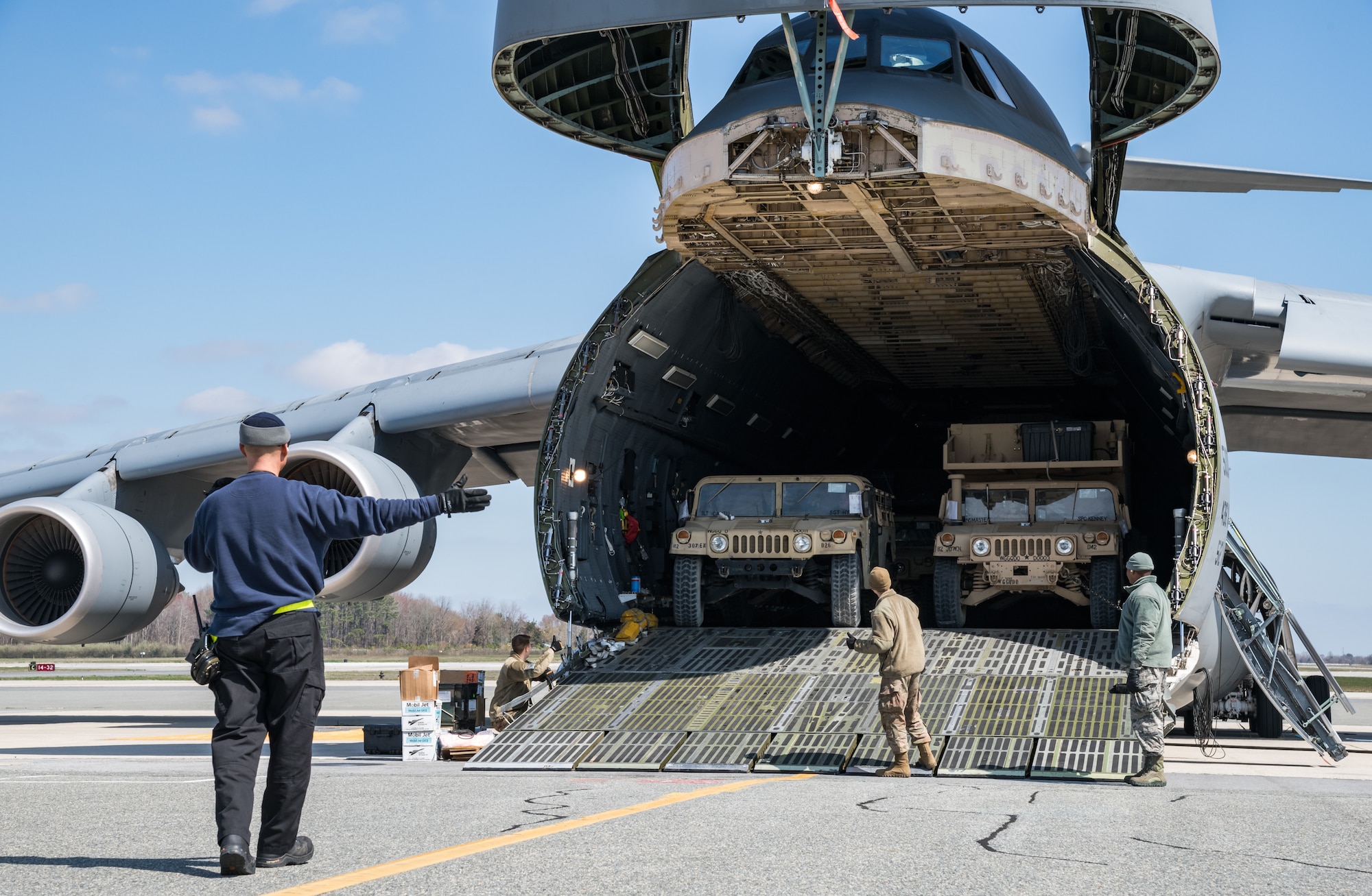 Dane Coward, left, 436th Aerial Port Squadron ramp supervisor, marshals a humvee down the forward loading ramp of a C-5M Super Galaxy March 26, 2020, at Dover Air Force Base, Delaware. Coward and his crew unloaded numerous Humvees off the Super Galaxy as required airlift operations continued during the evolving COVID-19 pandemic (U.S. Air Force photo by Roland Balik)