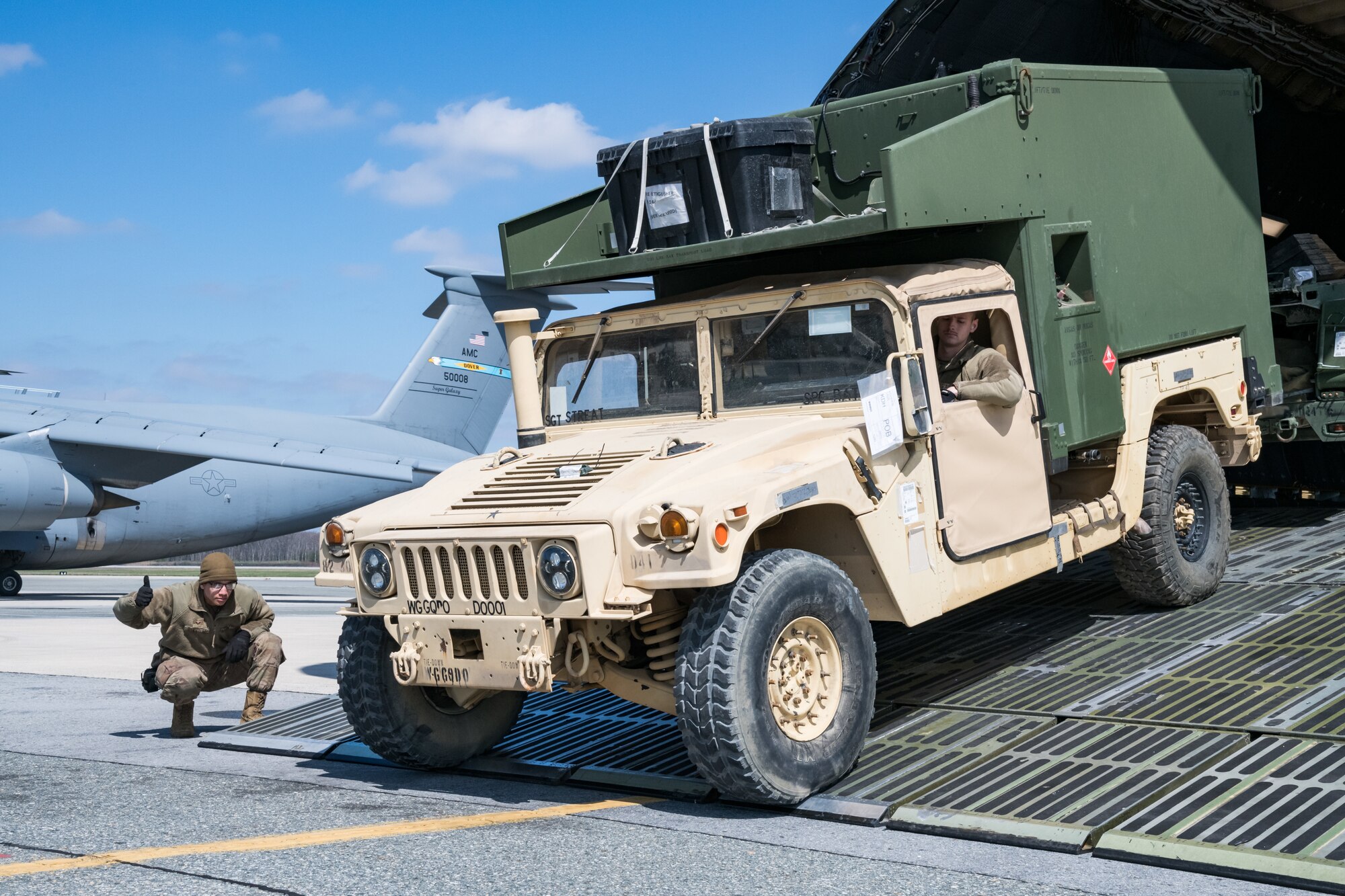 Senior Airmen Terry Brantley, left, clears Cody Kuszajewski, both 436th Aerial Port Squadron ramp specialists, to drive a humvee down the forward loading ramp of a C-5M Super Galaxy, March 26, 2020, at Dover Air Force Base, Delaware. Brantley, Kuszajewski and other 436th APS members unloaded numerous humvees off the Super Galaxy as required airlift operations continued during the evolving COVID-19 pandemic. (U.S. Air Force photo by Roland Balik)
