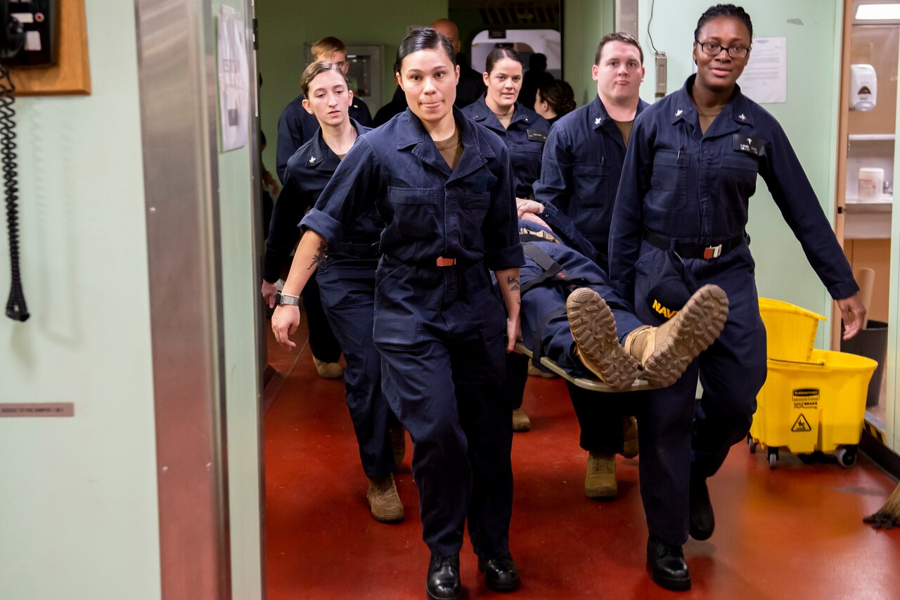 Sailors bear body on a stretcher.