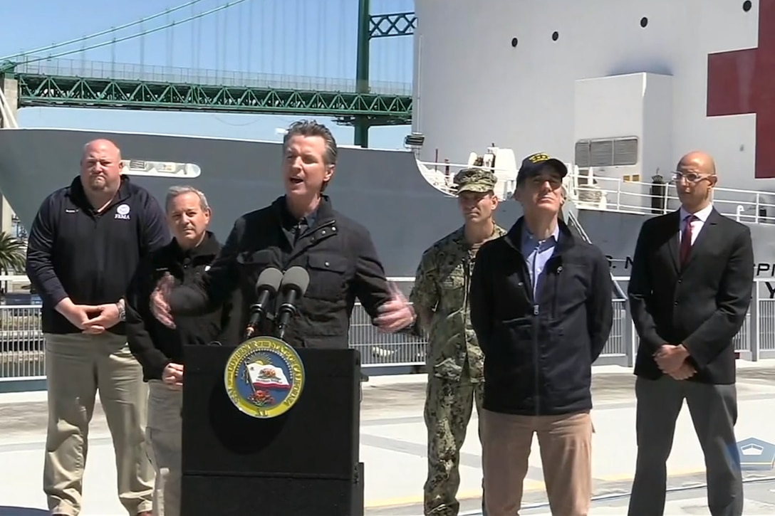 Men at lectern gestures while speaking to an audience.