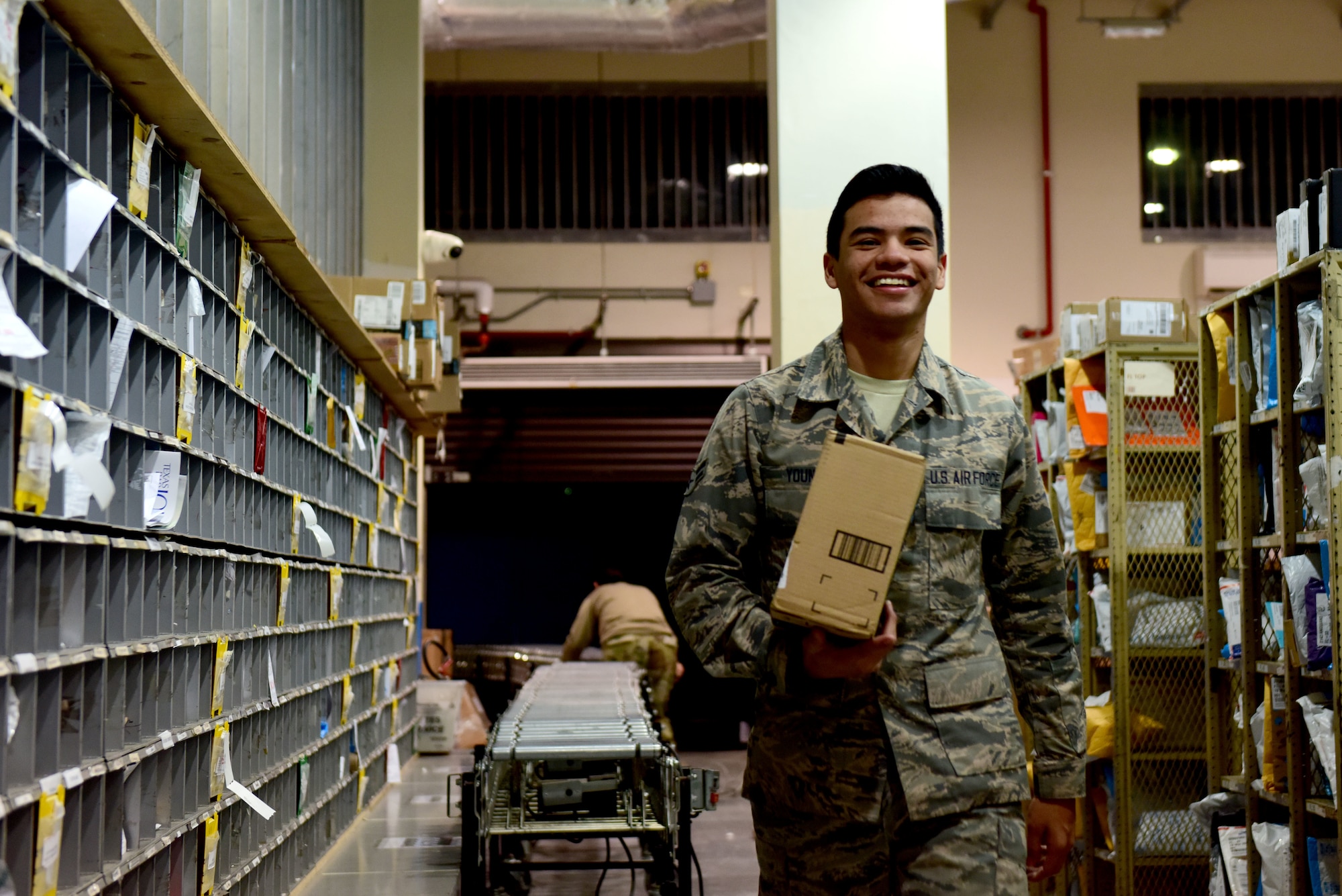 U.S. Air Force Airman 1st Class Daniel Young, 31st Force Support Squadron postal clerk, transfers a package from sorting to the shelf at the Aviano Post Office, Aviano Air Base, Italy, March 25, 2020. Due to the recent surge of arrivals, the post office has had full shelves and an abundance of packages awaiting pickup. (U.S. Air Force photo by Staff Sgt. Kelsey Tucker)