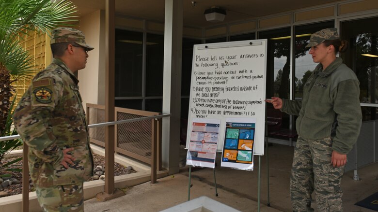 A photo of an Airman pre-screening a medical facility visitor before allowing him entrance