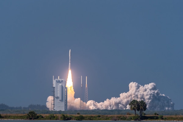 A rocket launches off a platform; smoke and flame appear underneath it.