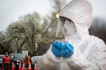 A nurse changes out gloves while New Jersey National Guard Airmen direct traffic at a COVID-19 Community-Based Testing Site at the PNC Bank Arts Center in Holmdel, N.J., March 23, 2020.