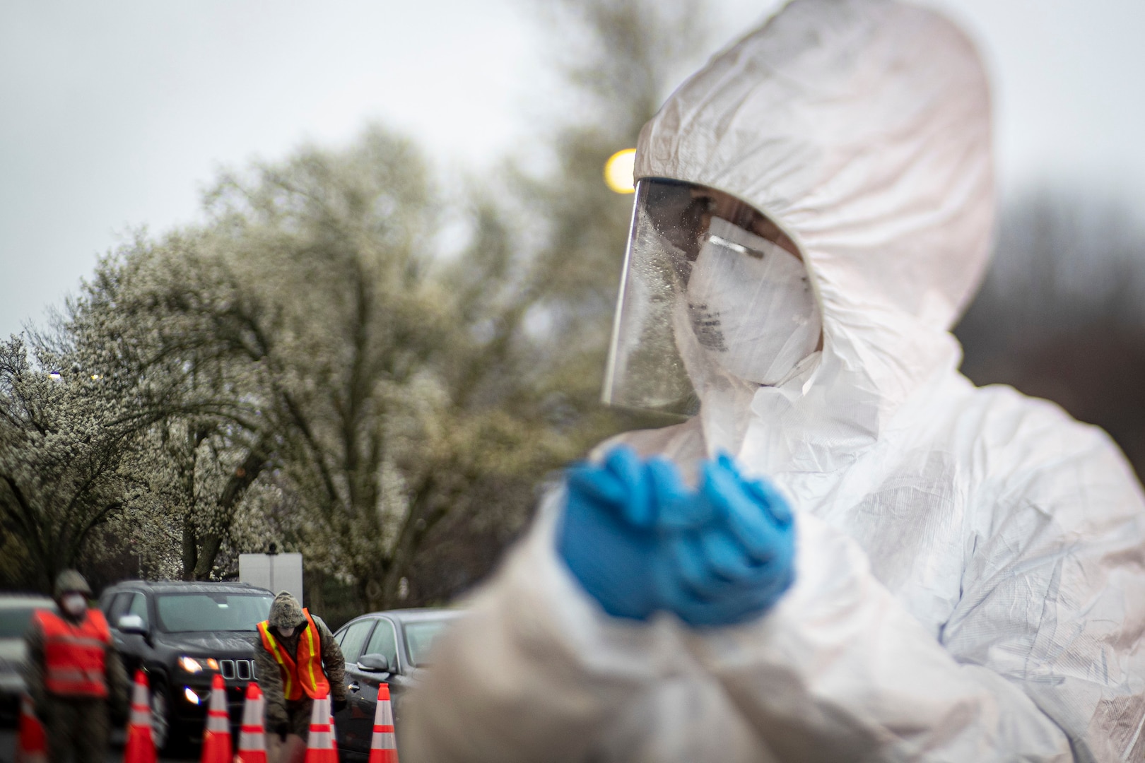 A nurse changes out gloves while New Jersey National Guard Airmen direct traffic at a COVID-19 Community-Based Testing Site at the PNC Bank Arts Center in Holmdel, N.J., March 23, 2020.