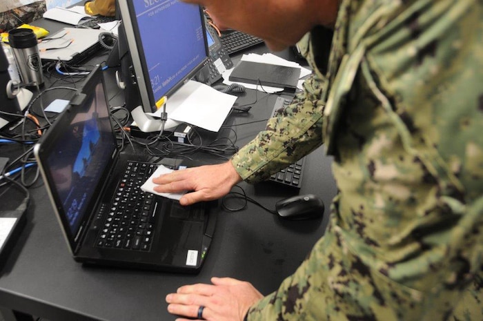 Senior Chief Petty Officer John Lynch, a naval reservist assigned to the International Maritime Security Construct (IMSC), uses disinfecting wipes to clean a workstation at the IMSC headquarters. The IMSC ensures freedom of navigation and free flow of commerce in international waters throughout the Arabian Gulf, Strait of Hormuz, the Bab el-Mandeb Strait, and the Gulf of Oman.