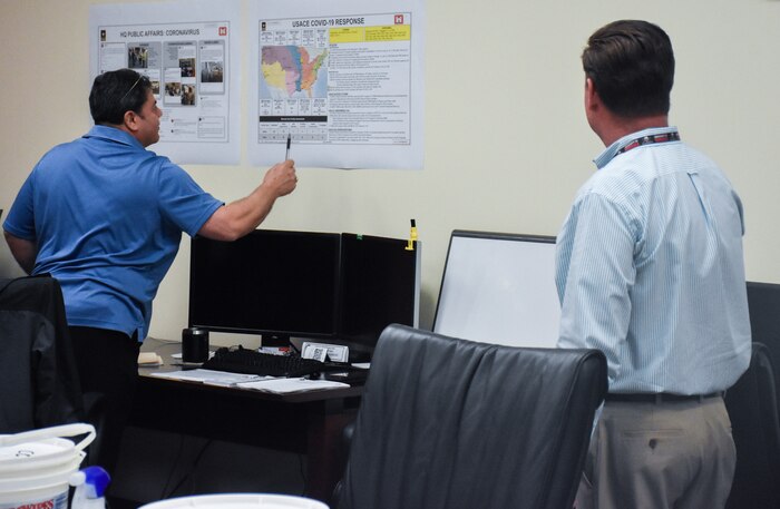 Antonio Santoscruz, (left) U.S. Army Engineering and Support Center, Huntsville Emergency Operations Center operations and plans specialist, refers to a chart of COVID-19 response effort information during an EOC meeting with James Buhr, EOC team member (right) March 25.