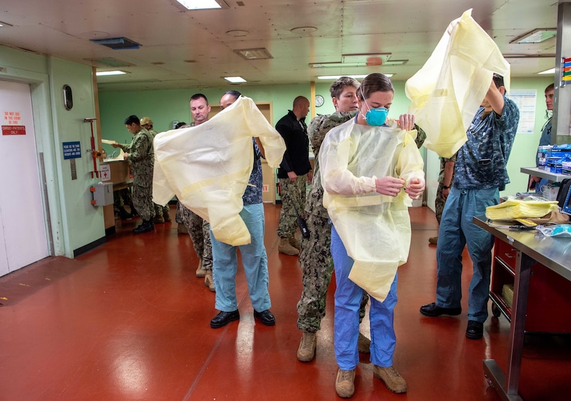 Three sailors put on surgical gowns.