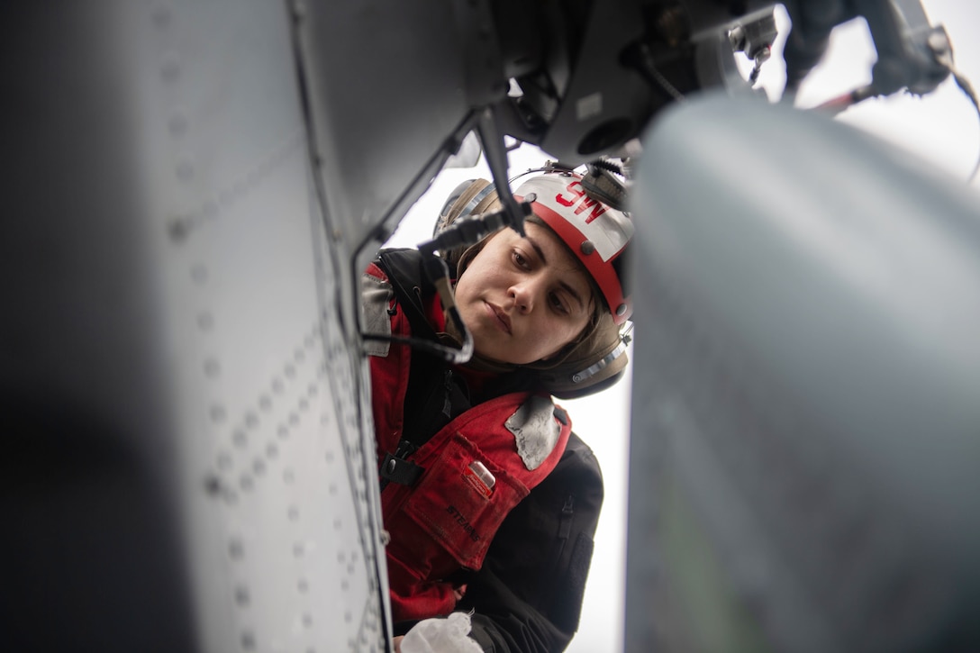 A sailor looks down at part of a helicopter.