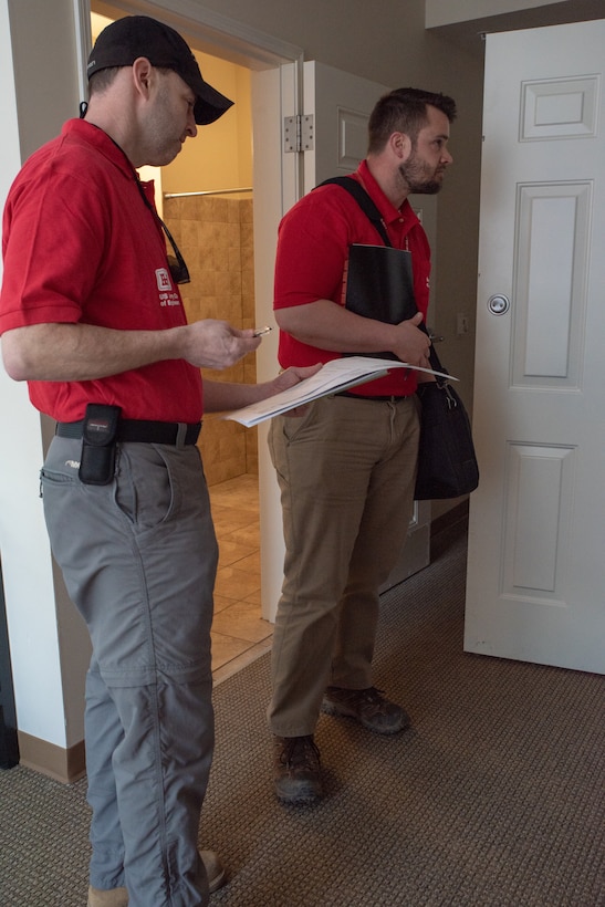 Two men wearing red polo shirts inspect a room.