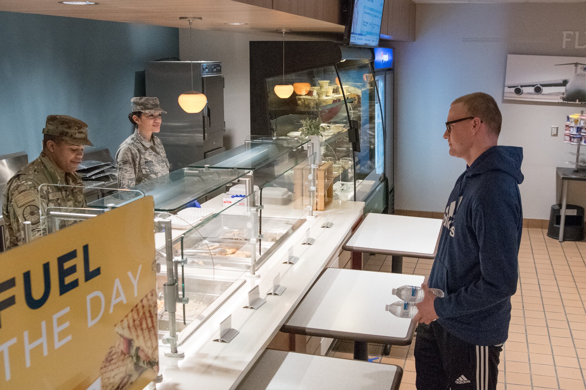 An Airman picks up lunch at the Patterson Dining Facility March 30, 2020, at Dover Air Force Base, Delaware. The 436th Force Support Squadron continues to provide meals for dormitory residences and essential personnel during the COVID-19 pandemic. The tables in front of the counter are meant to help enforce social distancing and mitigate the spread of COVID-19. (U.S. Air Force photo by Mauricio Campino)