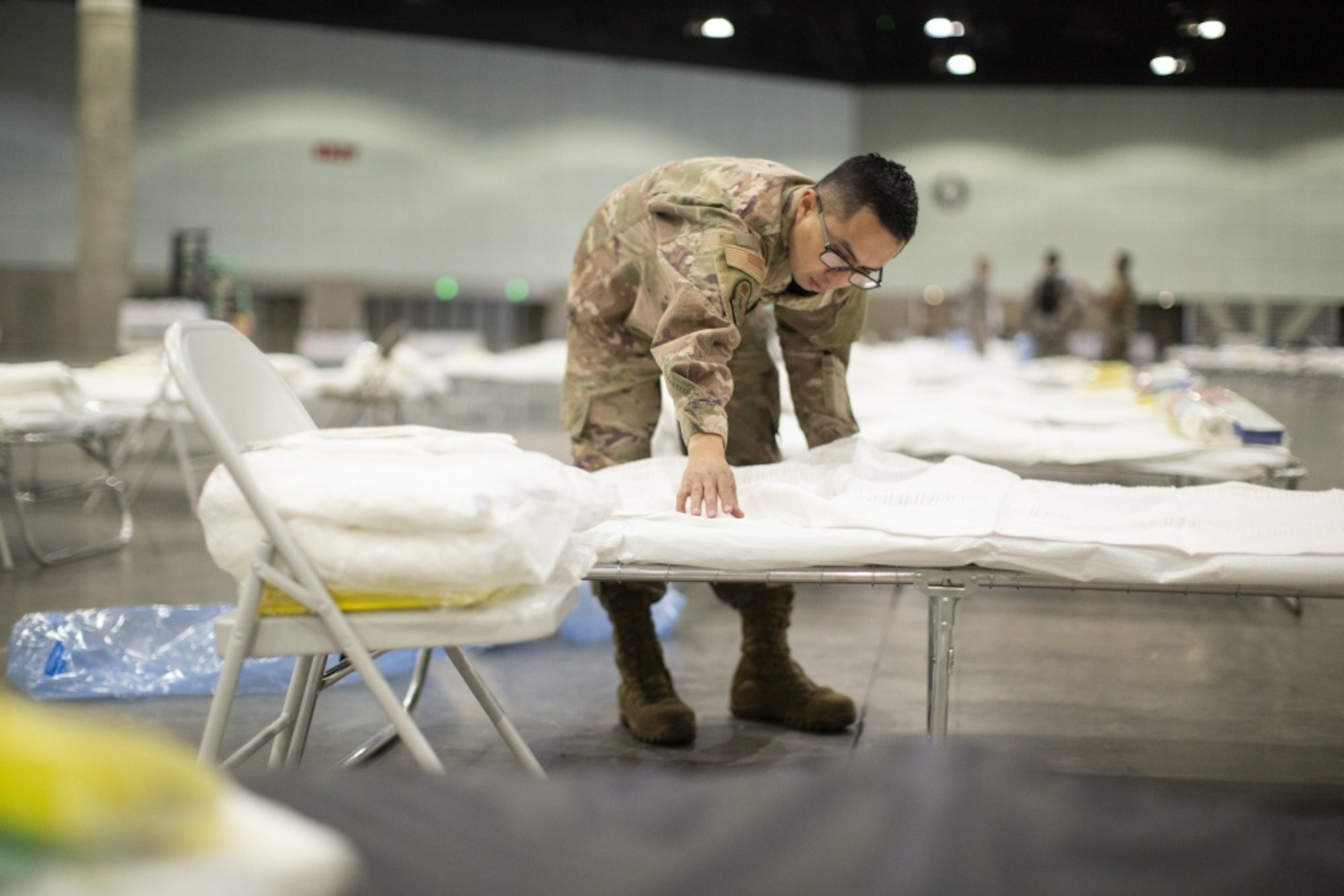 A photo of U.S. Air National Guard Mario Lopez-Casas putting sheets on a hospital bed inside the Los Angeles Convention Center.