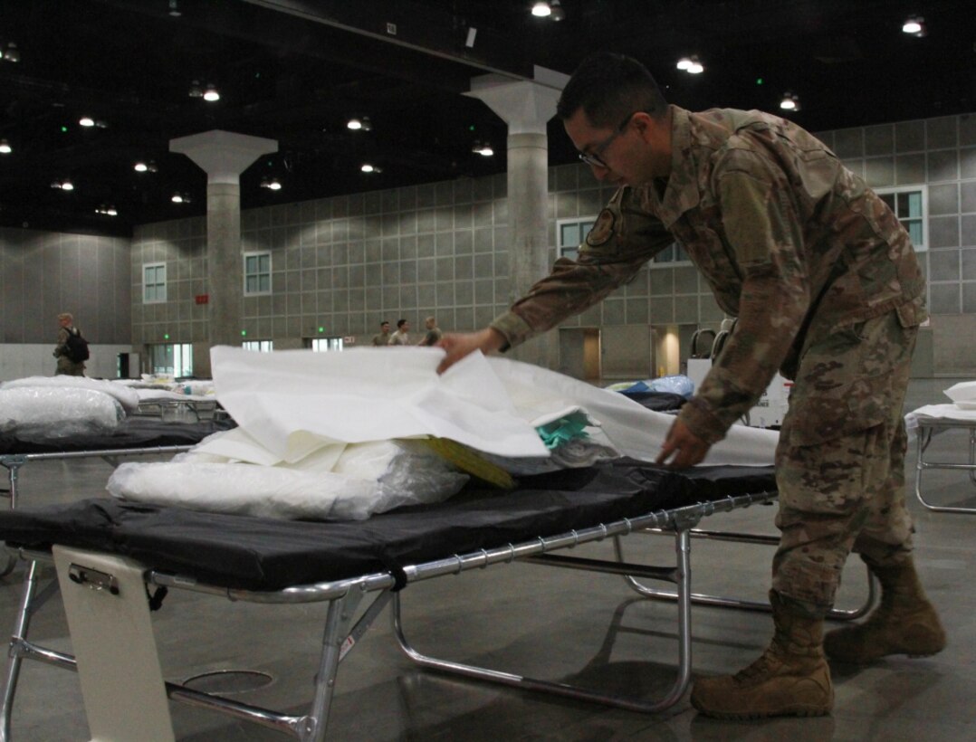 A photo of U.S. Air National Guard Tech. Sgt. Mario Lopez-Casas making a temporary hospital bed inside the Los Angeles Convention Center.