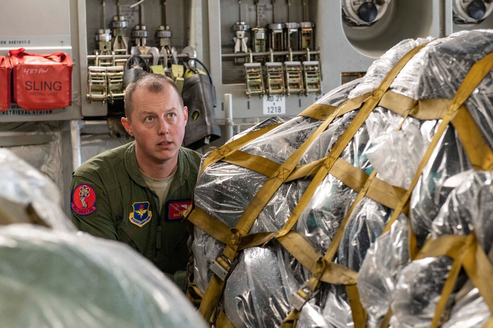 Airman sitting inside airplane next to pallet of duffel bags