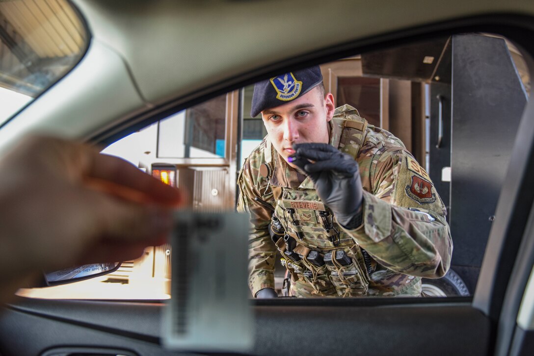 Senior Airman Jacob Stevens, 100th Security Forces Squadron defender, checks a member’s identification credentials at the gate while adhering to social distancing requirements on RAF Mildenhall, England, March 25, 2020. Personnel on base have taken extra precautions to prevent the spread COVID-19. (U.S. Air Force photo by Staff Sgt. Luke Milano)