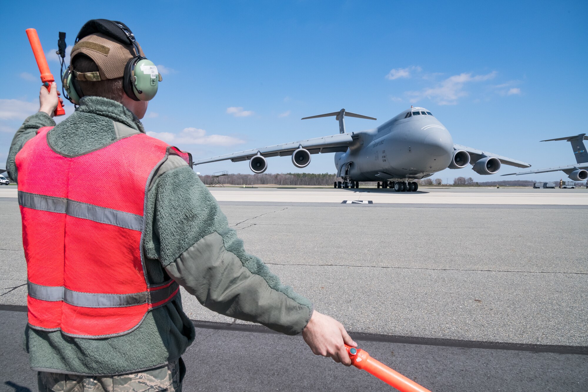 Senior Airman Jeffrey Mazzotta, 436th Aircraft Maintenance Squadron hydraulics journeyman, marshals a C-5M Super Galaxy off it's parking spot March 26, 2020, on Dover Air Force Base, Delaware. Mazzotta and other members of his launch crew wore approved Operational Camouflage Pattern (OCP) bump caps and observed social distancing practices, while performing maintenance on the Super Galaxy. (U.S. Air Force photo by Roland Balik)