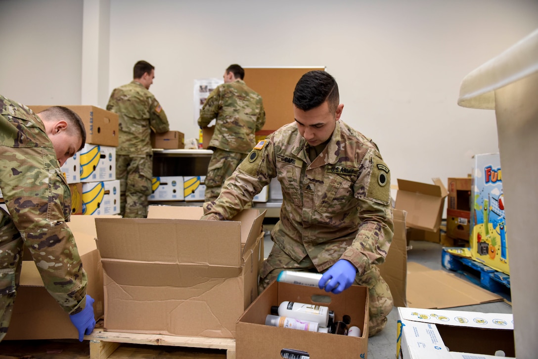Soldiers wearing blue gloves place donated items into boxes.