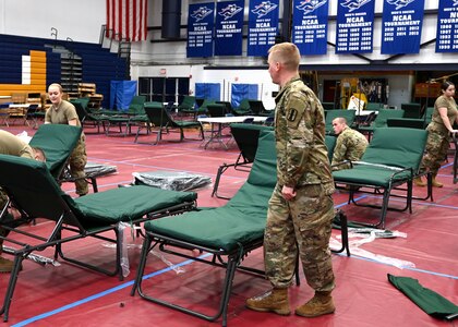Soldiers set up cots in a gym.