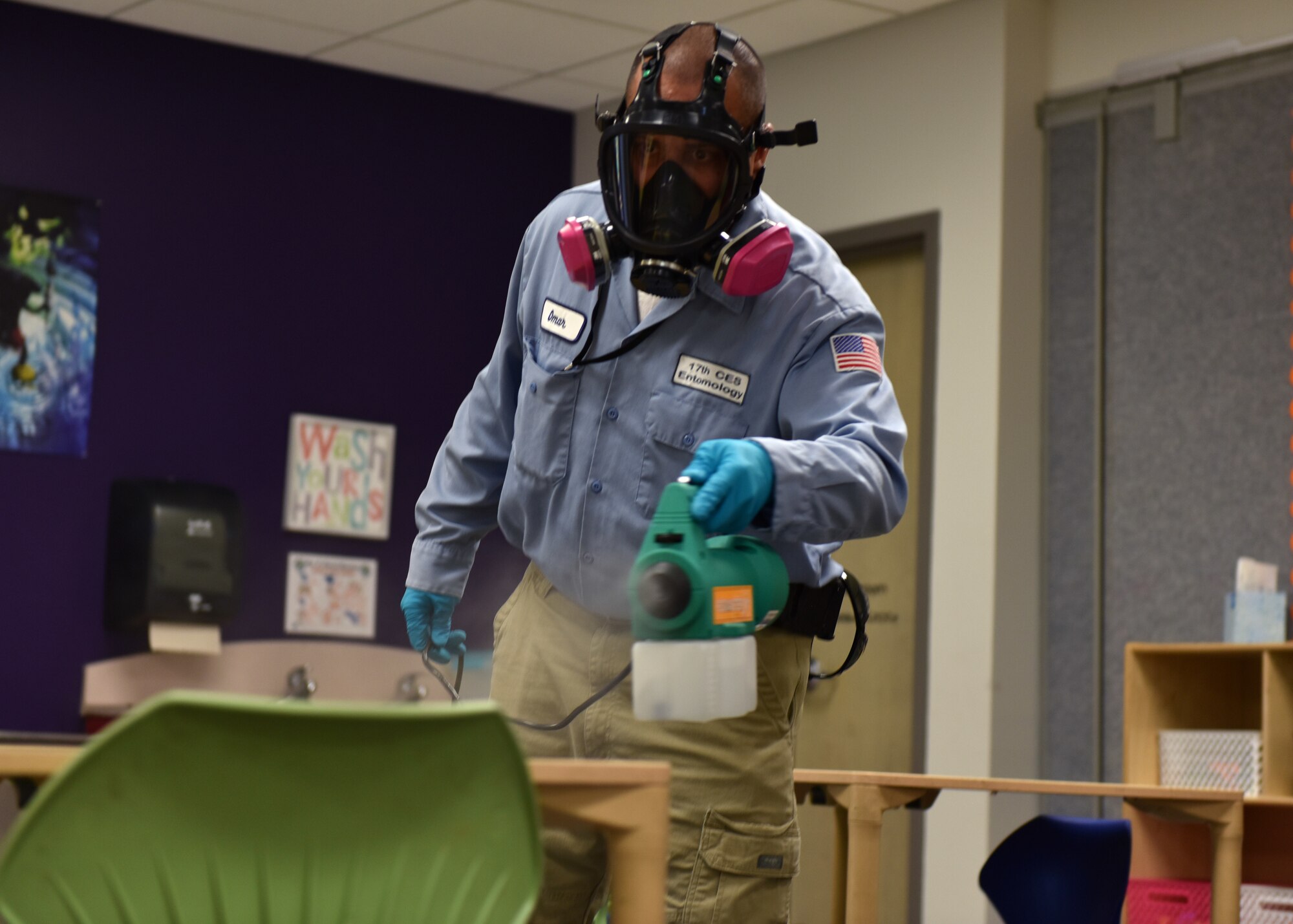 17th Civil Engineer Squadron Pest Controller Omar Martinez, walks around a classroom dispersing a disinfectant mist on all surfaces at Goodfellow Air Force Base, Texas, March 30, 2020. The chemical used is 99 percent effective at bonding to germs on the surface and killing them within the dwell time of 20 minutes. (U.S. Air Force photo by Senior Airman Seraiah Wolf)
