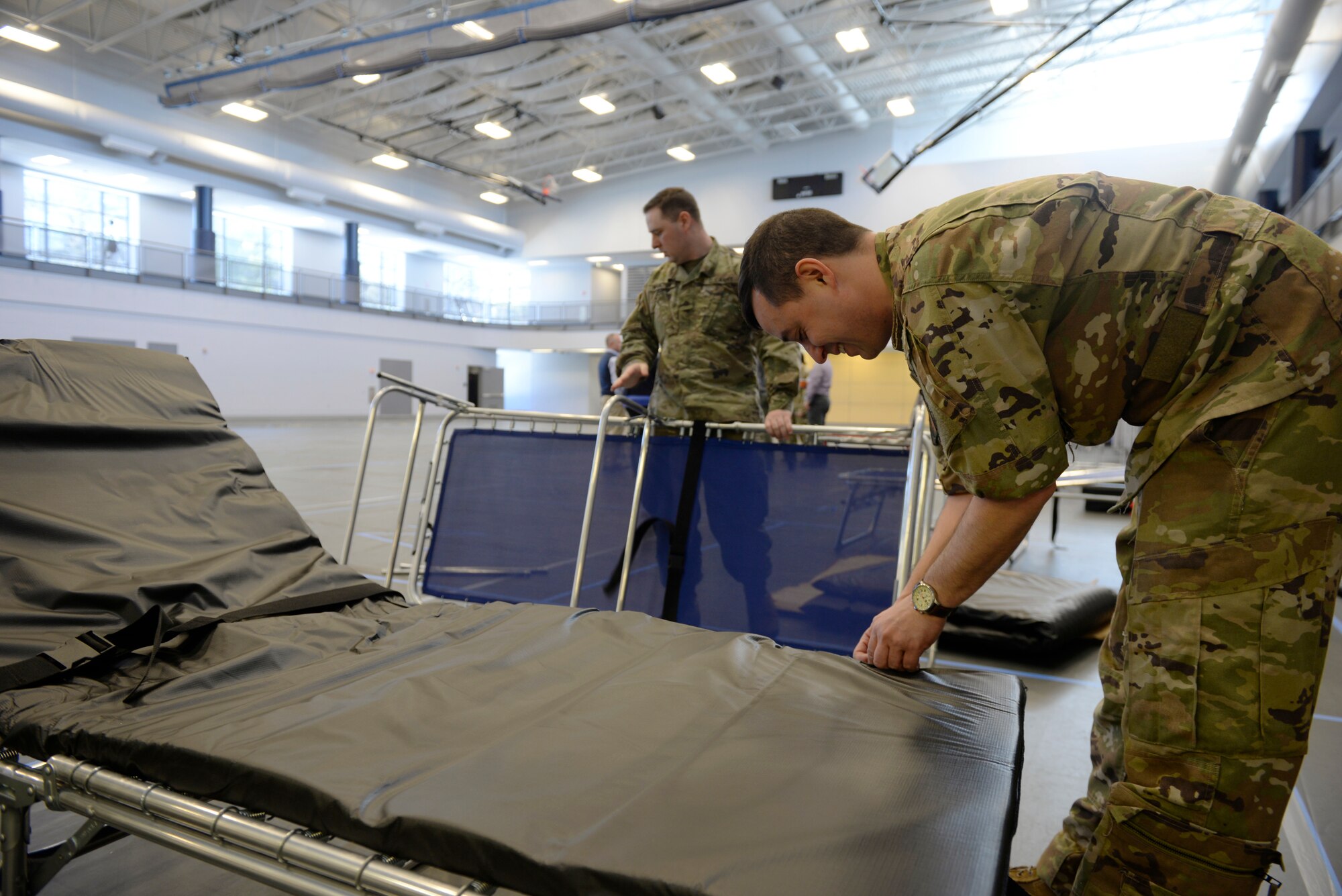 Capt. Jacob Ricciotti, foreground, a pilot for the 133rd Air Refueling Squadron, New Hampshire Air National Guard, and Pfc. Nathan Huston, a diesel mechanic for the 197th Field Artillery Brigade, New Hampshire Army National Guard set up beds at the Hamel Recreational Center at the University of New Hampshire in Durham, Mar. 23. The facility in Durham will augment area hospitals treating COVID-19 cases, if necessary. It is one of nine "surge" locations the NH Guard, in coordination with local and state healthcare agencies, plans to set up and manage across the state. (U.S. Air National Guard photo by Tech. Sgt. Aaron Vezeau)