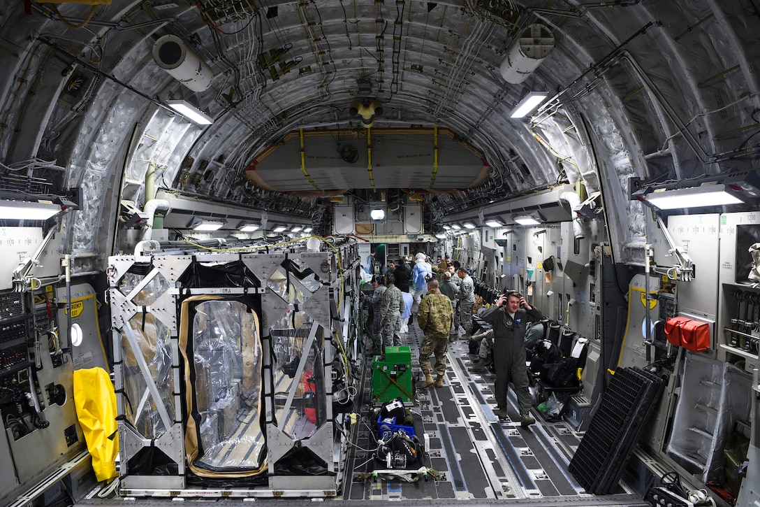 The cargo hold of an aircraft carries several large, metal containers with plastic sheeting for windows.