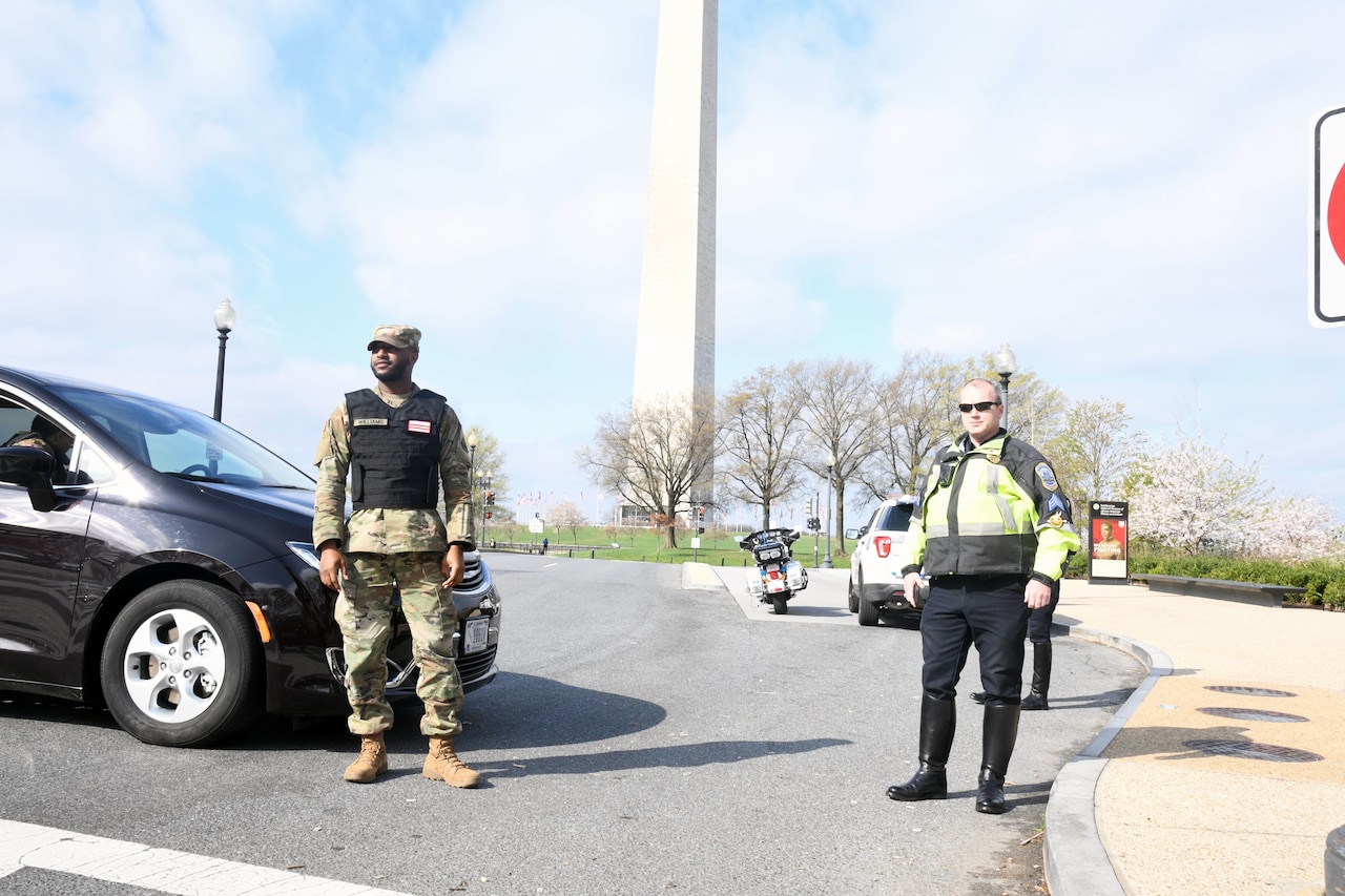 Men in uniform stand in an empty street with the Washington Monument in the background.