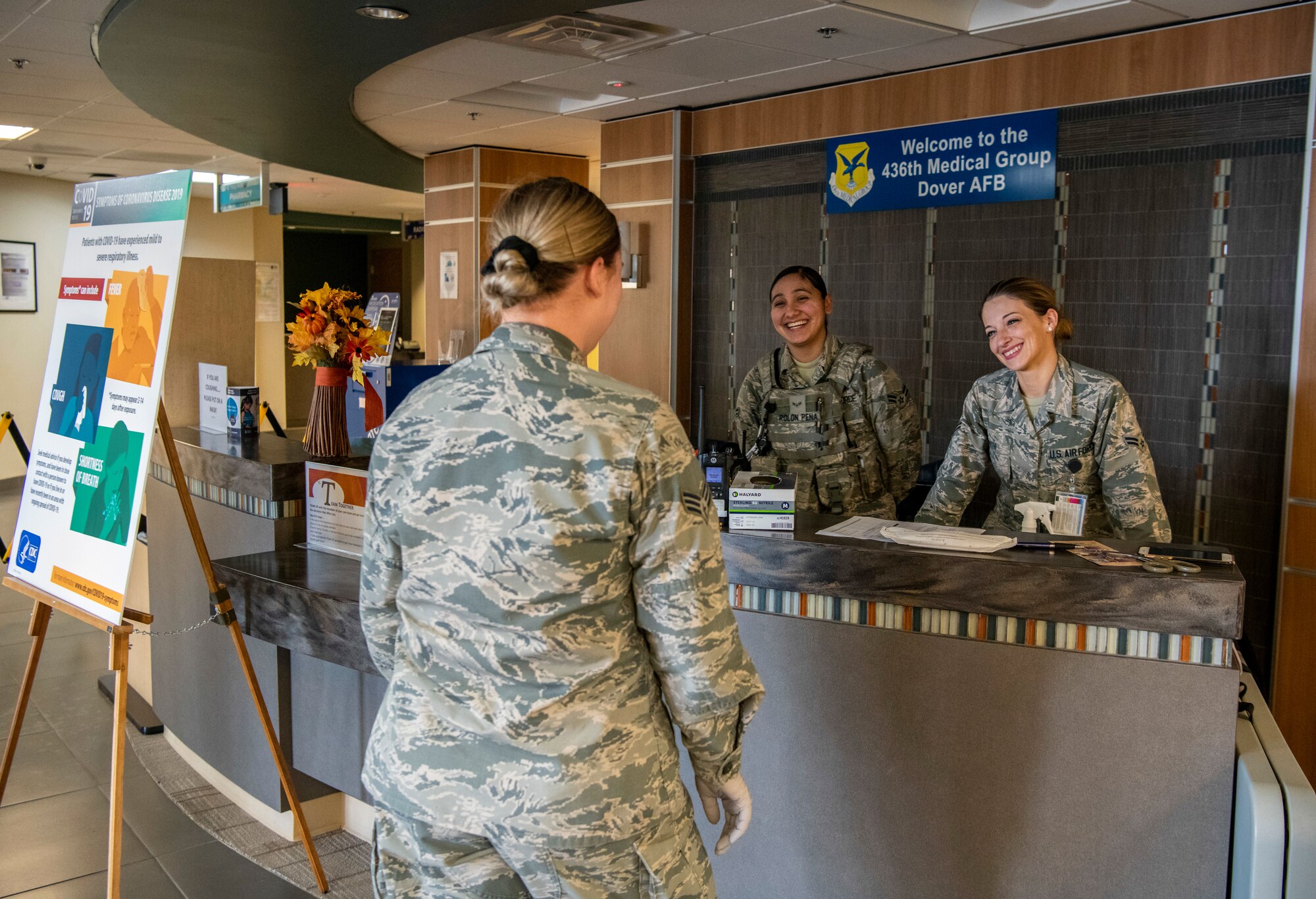 Airman 1st Class Guadalupa Rolon Pena, 436th Security Forces Squadron response force member (middle), and Airman 1st Class Kathleen Smith (right), 436th Health Care Operations Squadron pediatric medical technician, help direct patients at the medical clinic’s front desk at Dover Air Force Base, Delaware, March 30, 2020. The medical clinic is sectioned off to help prevent any spread of illnesses. Dover AFB medical personnel continue to provide care for Airmen and their families, while supporting state and national response efforts.  (U.S. Air Force photo by Senior Airman Christopher Quail)