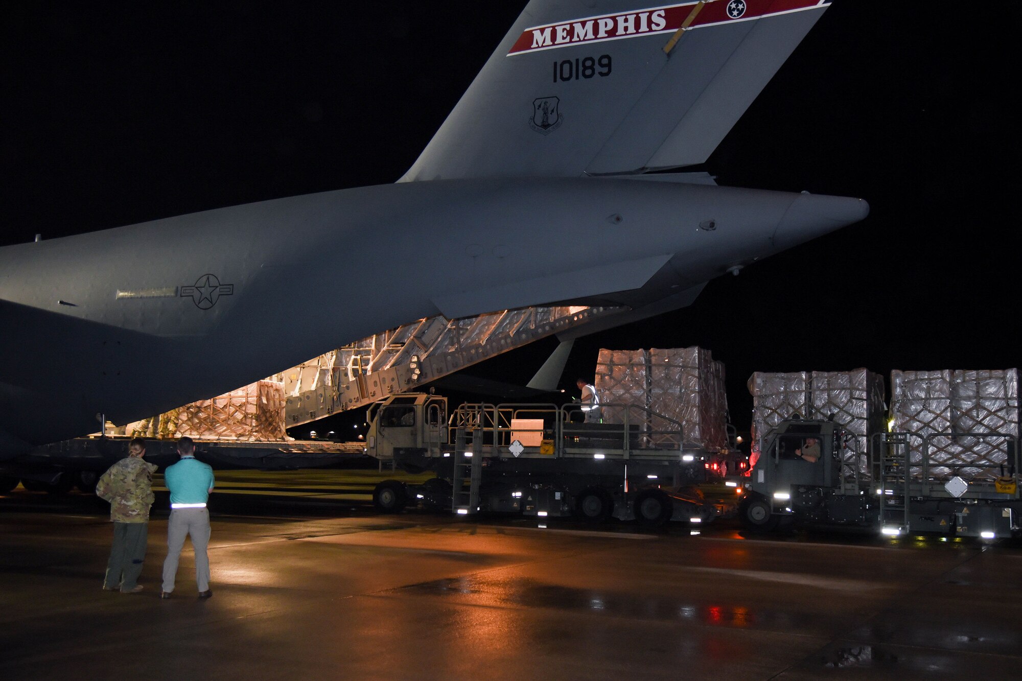 A vehicle unloads pallets from a military aircraft.