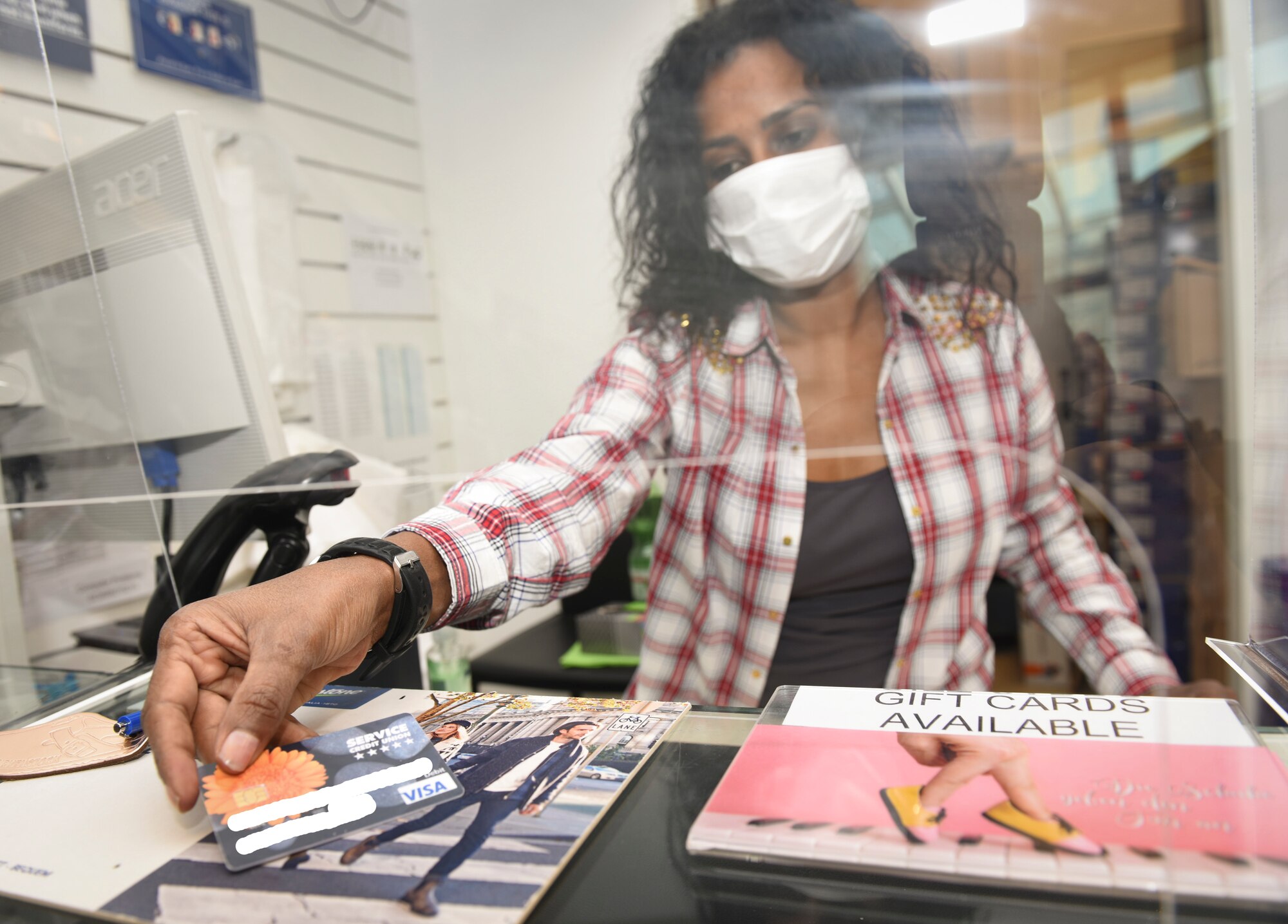 Yordanos Ghirmay, Army and Air Force Exchange Service cashier, accepts payment through an acrylic glass shield at the Base Exchange at Ramstein Air Base, Germany, April 21, 2020