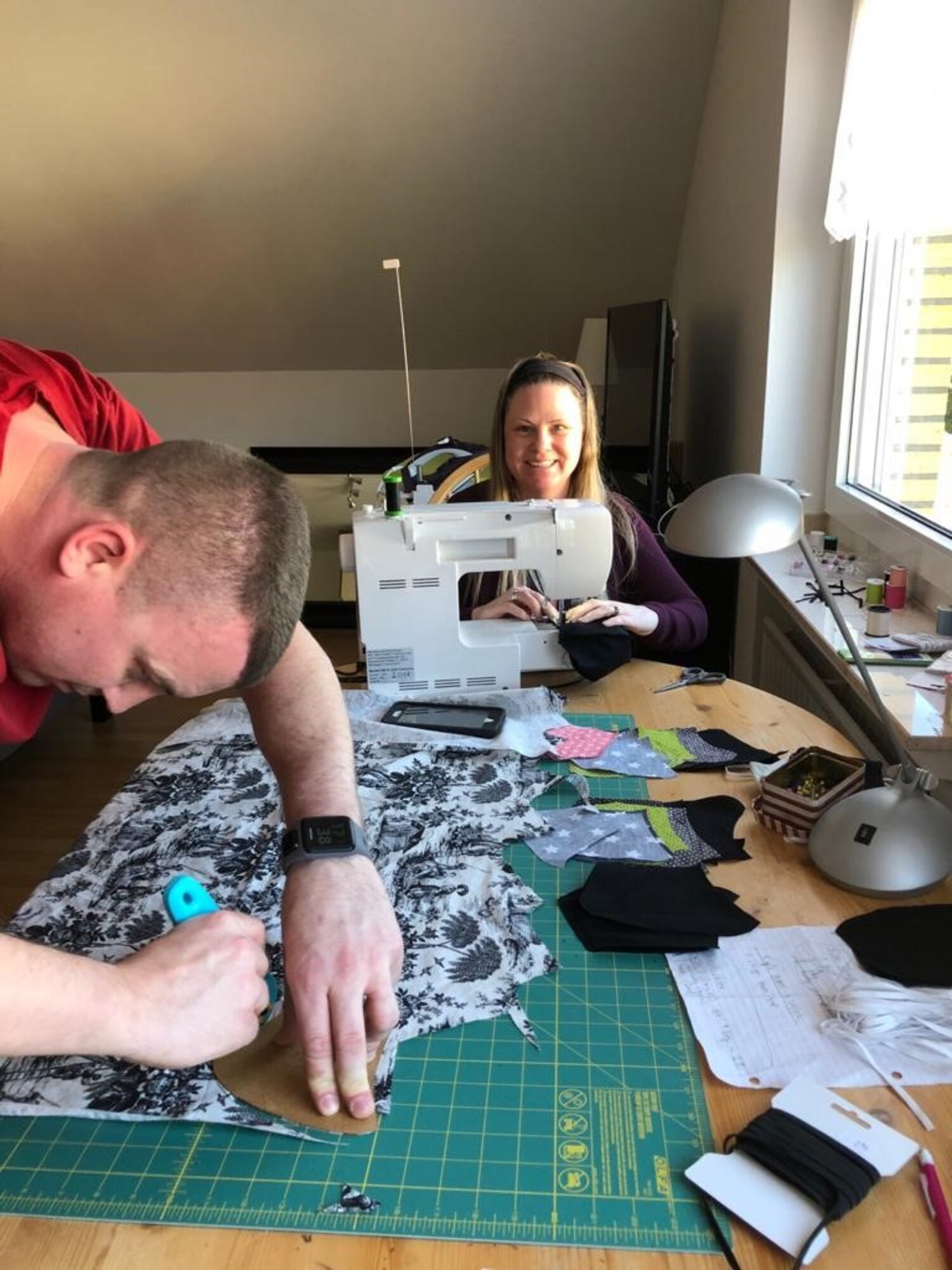 U.S. Air Force Tech. Sgt. Cameron Green, 470th Air Base Squadron paralegal, left, and his wife Katie, right, cut and sew masks for the 470th Air Base Squadron in Geilenkirchen, Germany, April 20, 2020. Sewing masks for the 470th ABS are the Green’s way of giving back to the community during the COVID-19 pandemic. (U.S. Air Force photo courtesy of Master Sgt. David Zamora-Alvarez)