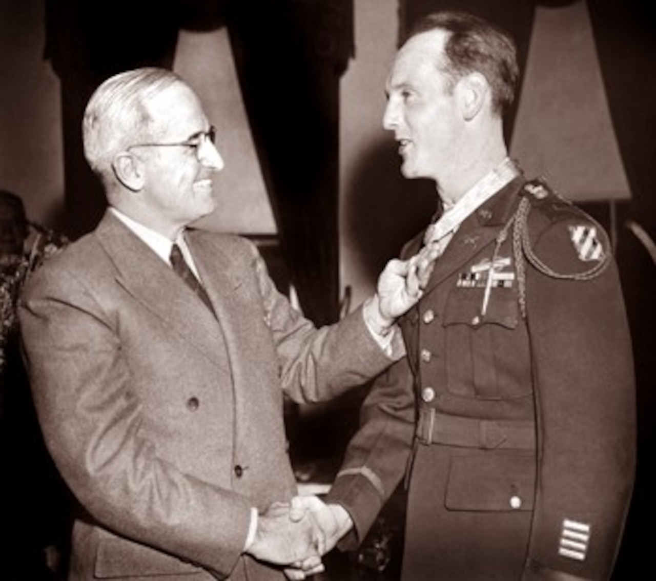 A man shakes the hand of a soldier with a medal around his neck.
