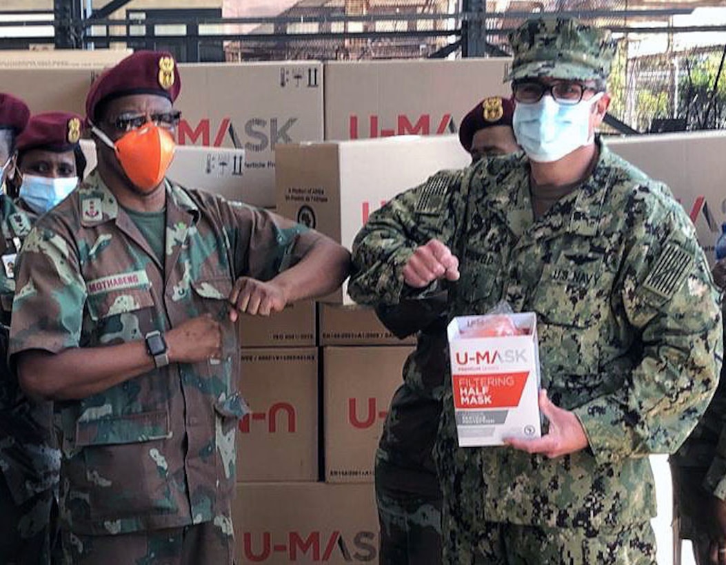 Service members from two nations are wearing personal protective equipment masks and greet each other with an elbow bump.