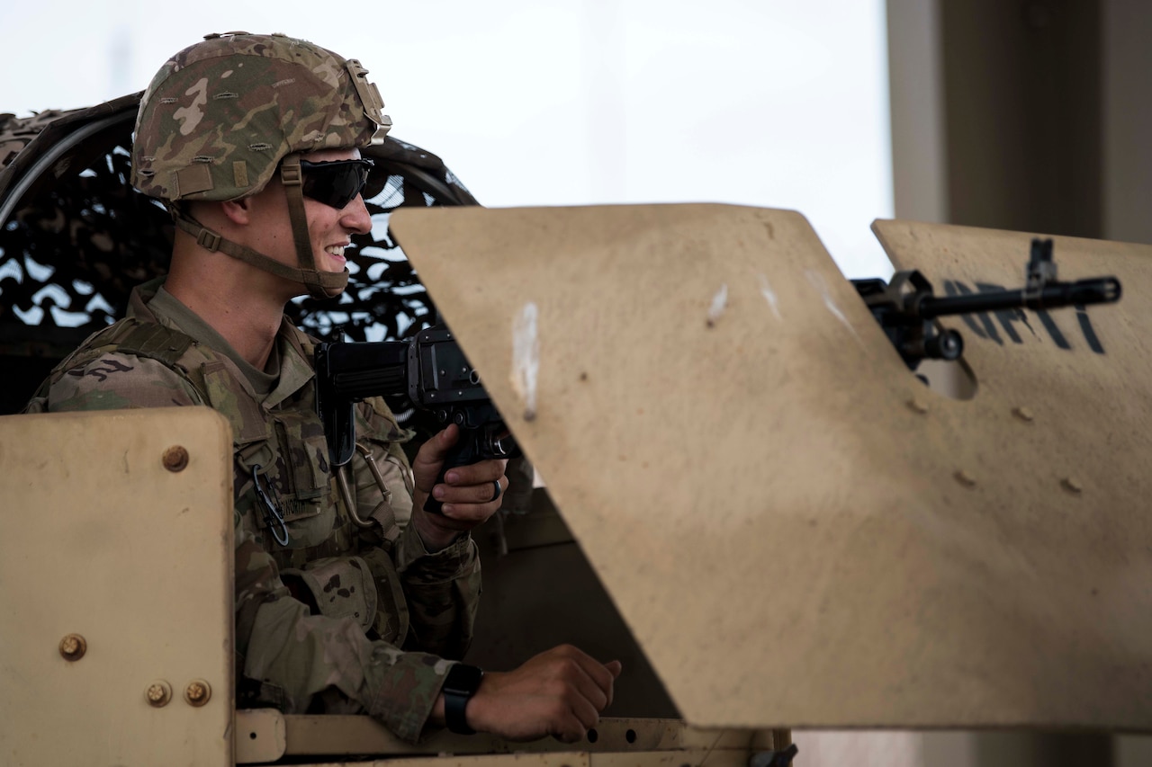 Soldier is in full battle gear in a Humvee holding a gun.