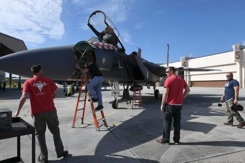 Photo shows four men working on an F-15 aircraft outside.