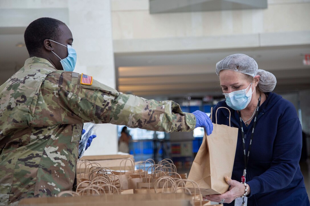 A soldier distributes a brown-bag meal to a medical technician. personnel