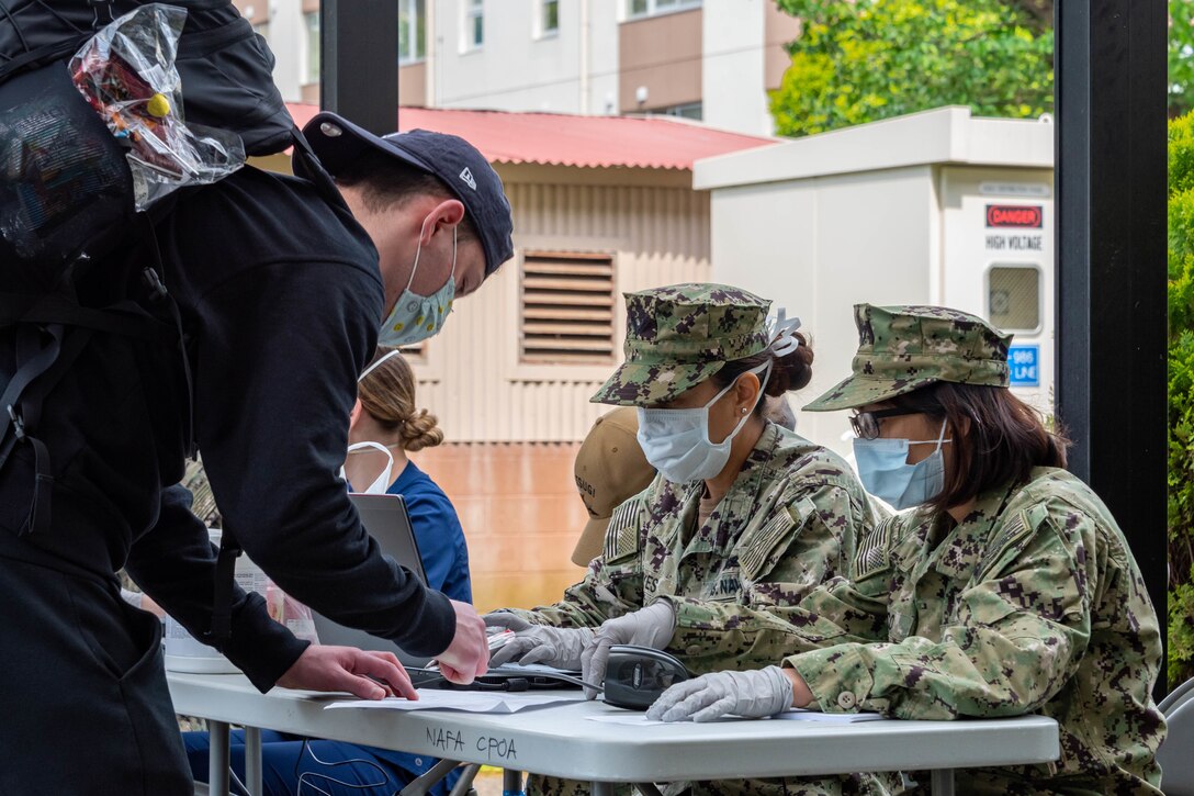 A sailor wearing a mask looks for his name on a sheet of paper.