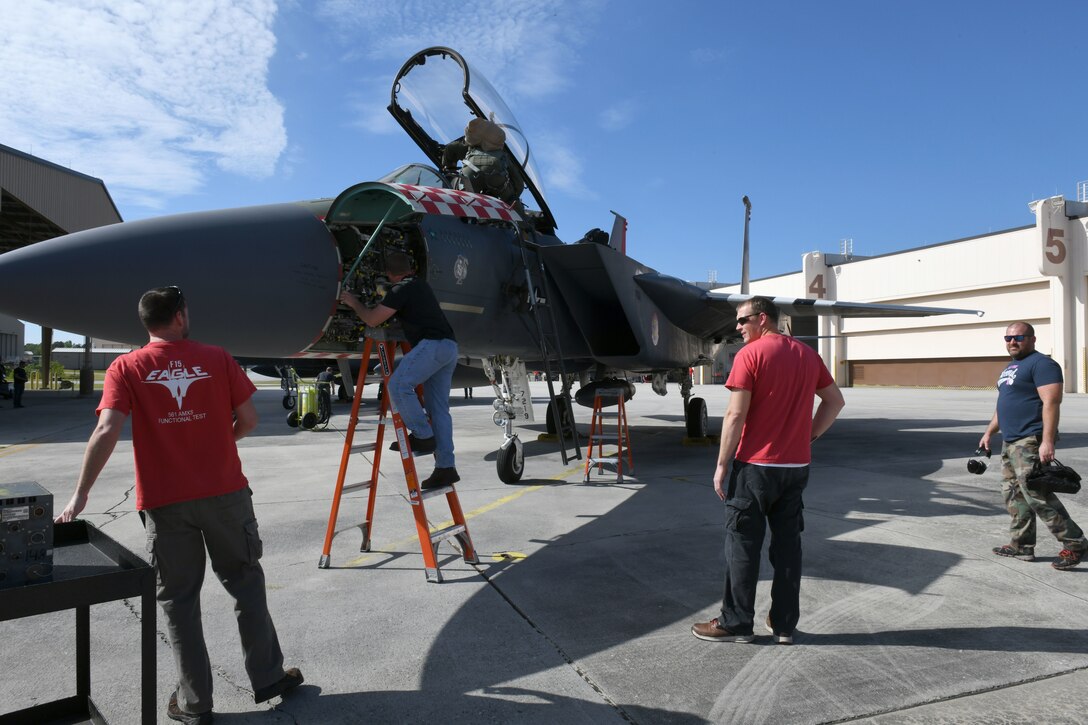 Photo shows four men working on an F-15 aircraft outside.