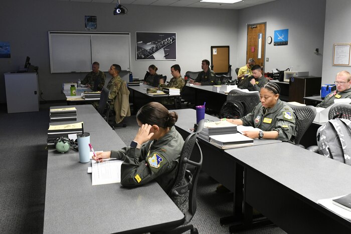 Photo shows multiple Airmen in a classroom setting reading notes at their tables.