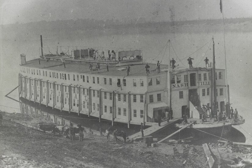 A Civil War-era steamship is docked along a river bank.